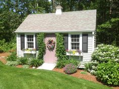 a small white house with pink door and window boxes on the outside, surrounded by greenery