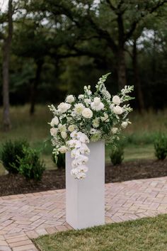 a white vase filled with flowers sitting on top of a brick walkway