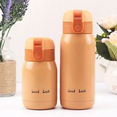 two orange insulated bottles sitting next to each other on a table with flowers in the background