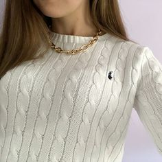 a woman wearing a white cable knit sweater with a gold chain around her neck and an embellished pony on the collar