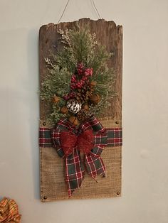 a wooden sign hanging on the wall decorated with pine cones, berries and evergreens