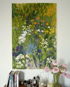 a painting is hanging on the wall above a table with flowers and other items in front of it