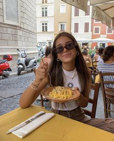 a woman sitting at an outdoor table eating pasta