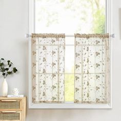 a window with sheer curtains and flowers on the curtain rod, in front of a white wall