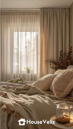 a bed with pillows and blankets on top of it next to a glass vase filled with flowers