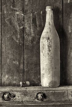 an old bottle sitting on top of a wooden box next to a wall with peeling paint