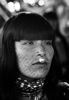 a woman with her face covered in wire and beads, looking at the camera while she is