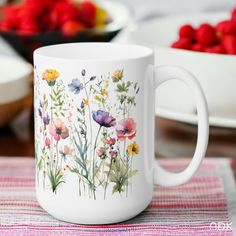 a white coffee mug with flowers painted on the side and strawberries in the background