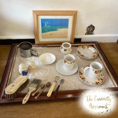 a tray with cups, saucers and brushes on top of a wooden table next to a painting