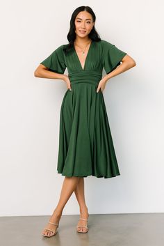 a woman in a green dress poses for the camera with her hands on her hips