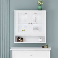 a white cabinet sitting on top of a dresser next to a green vase with flowers