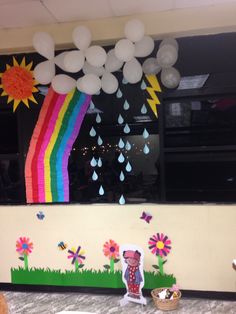 a table topped with paper flowers and balloons in front of a rainbow wallpapered window