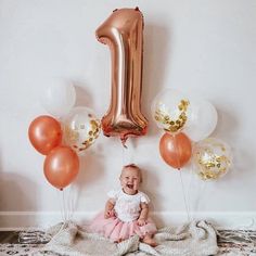 a baby is sitting on the floor with balloons and a number one balloon in front of her