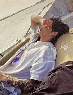 a man laying on top of a boat next to the ocean with his eyes closed