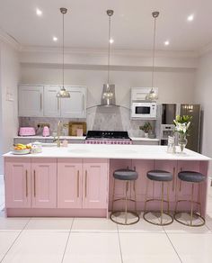 a kitchen with pink cabinets and stools in front of the counter top, along with white tile flooring