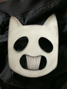 a white mask with black eyes and mouth is shown in front of a black jacket