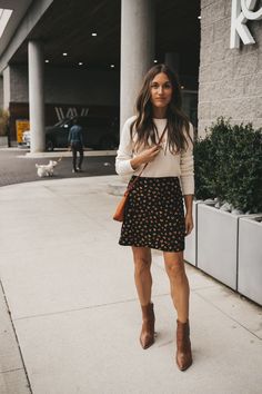 ashley wearing a cream colored crewneck sweater, black floral mini skirt and brown boots standing next to a gray building Stylish Capsule Wardrobe, Balanced Living, Effortless Beauty, Neutral Style