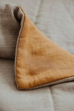 the corner of an unmade bed with linens on it and a brown pillow