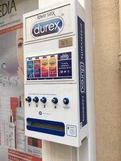 a close up of a vending machine near a wall with advertisements on it and an advertisement for durex in the background