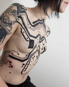 a woman with black ink on her body and chest is standing in front of a white wall