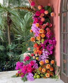 colorful flowers are growing up the side of a pink building with palm trees in the background