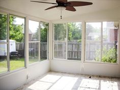 an empty room with three large windows and a ceiling fan in the middle of it