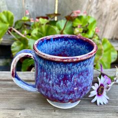 a close up of a cup on a wooden table with flowers in the back ground