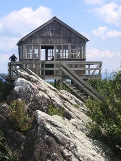 a house on top of a mountain with stairs leading up to it and people standing at the top