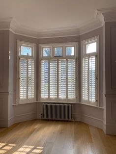 an empty room with wooden floors and white shutters on the windows, along with a radiator