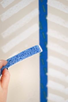 a hand holding a blue sponge in front of a wall with white paint on it