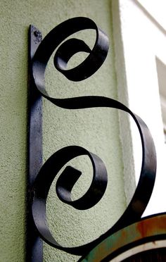 a metal sign mounted to the side of a green wall next to a clock tower