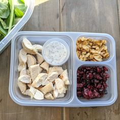 a plastic container filled with food on top of a wooden table next to a salad