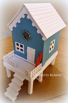 a paper model of a blue house with white sidings and a clock on the wall