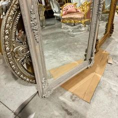 a large mirror sitting on top of a floor next to a pile of boxes and chairs