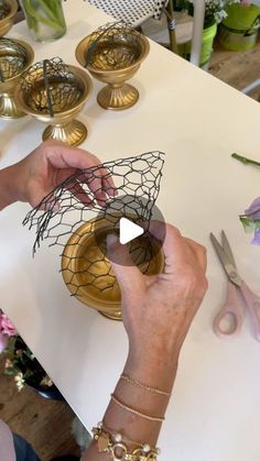 a woman is working with wire on a piece of paper next to flowers and scissors