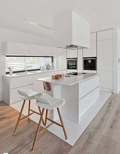 a white kitchen with two stools in front of the island and an oven on the wall