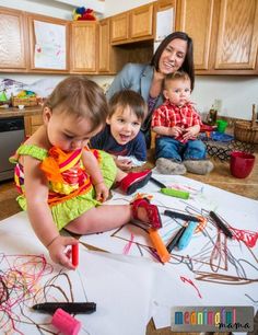 a woman and two children sitting on the floor with crayons in front of them