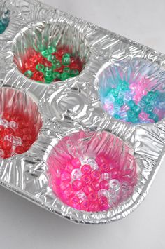 four plastic bowls filled with different colored beads on top of a silver foil tray that is sitting on a white surface