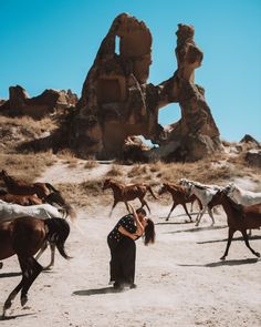 a woman standing in the middle of a desert with horses running around her and rocks in the background