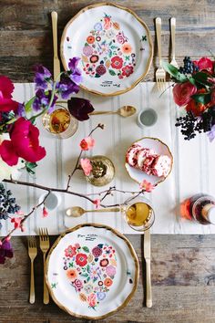 the table is set with plates, silverware and colorful flowers on it's placemats