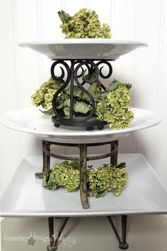 three tiered cake stand with green flowers on each tier and an iron base for the top