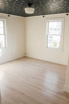 an empty room with two windows and hard wood flooring on the far wall is a painted ceiling