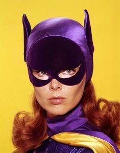 a woman wearing a purple mask and yellow cape with red hair in front of a yellow background