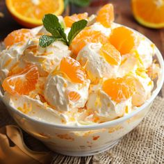 a bowl filled with oranges and whipped cream on top of a table next to sliced oranges