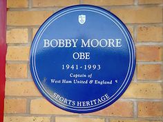 a blue plaque on the side of a brick building that says bobby moore obe