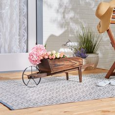 a wooden wheelbarrow with flowers in it sitting on a rug next to a chair