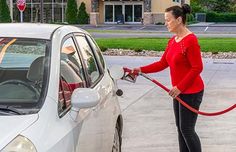 a woman pumping gas into her car with a red hose attached to the front door