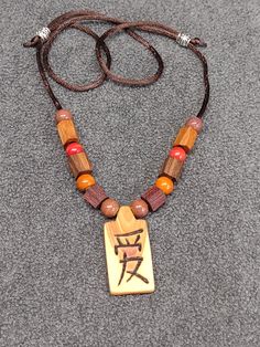 This item 977 is a hand made lilac pendant with woodburned love character.  Pendant is 1-1/2" x 3/4" x 3/16" and is on adjustable coffee colored silk cord along with handmade walnut, cherry, and purpleheart wood as well as ceramic beads, adjusts to 28" overall length simply by sliding the metal beads along the cord. The pendant and wooden beads were saturated with mineral oil and then wiped clean with the pendant then being waxed and polished with beeswax and orange oil.  You can wear this unique item proudly, knowing it is one of a kind! Casual Wooden Jewelry As A Gift, Love Character, Wood And Ceramic, Orange Oil, Silk Cord, Coffee Colour, Ceramic Beads, Mineral Oil, Metal Beads