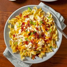 a plate of pasta with chicken, bacon and green onions on it next to a bowl of soup