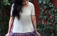 a woman with long black hair wearing a white shirt and plaid skirt